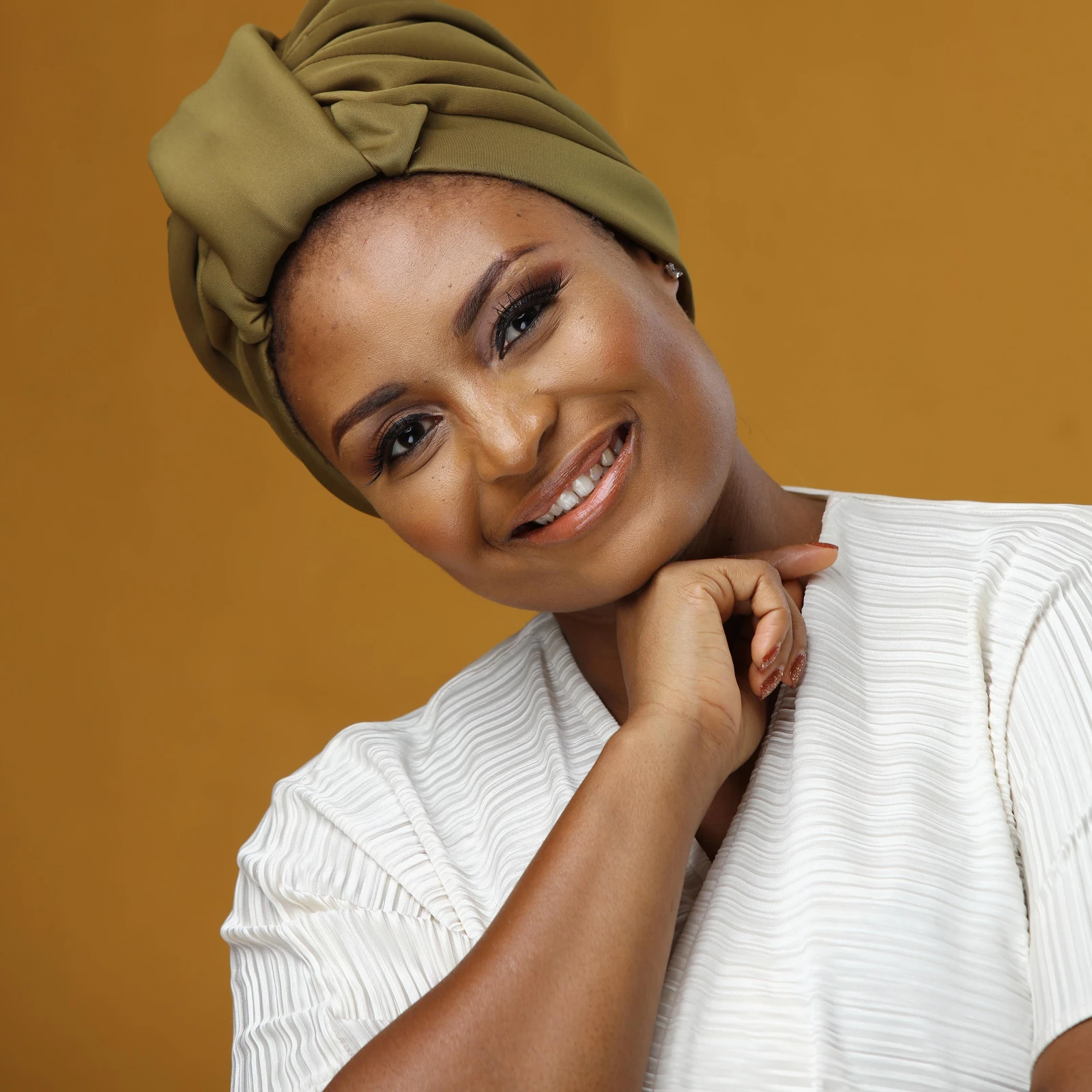 Smiling woman in an olive headwrap and a cream pleated top